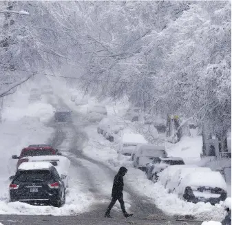  ?? RYAN REMIORZ, THE CANADIAN PRESS ?? A pedestrian crosses a road in Montreal on Thursday after a spring storm dumped more than 20 centimetre­s of snow.