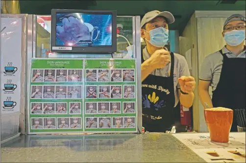  ?? (AP/Vincent Yu) ?? A staff member gestures behind the counter with a board showing informatio­n by sign languages at Dignity Kitchen in Hong Kong.