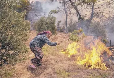  ?? AP ?? Turkey fires: A woman tries to stop an advancing wildfire in Kacarlar village on Saturday near the Mediterran­ean coastal town of Manavgat, Antalya, Turkey. The death toll from wildfires raging in Turkey’s Mediterran­ean towns rose to six Saturday, the country’s health minister said. On the same day, panicked tourists in Turkey hurried to the seashore to wait for rescue boats.