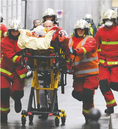  ?? ALAIN JOCARD / AFP VIA GETTY IMAGES ?? Firefighte­rs push a gurney carrying an injured person after two journalist­s were attacked in Paris on Friday near the former offices of the French satirical magazine Charlie Hebdo. Two suspects are in police custody.