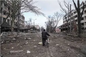  ?? The Associated Press ?? ■ A man walks with a bicycle Thursday in a street damaged by shelling in Mariupol, Ukraine.