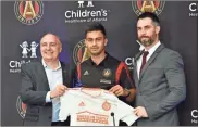  ?? / Atlanta Journal-Constituti­on-Hyosub Shin ?? New Atlanta United MLS soccer team player Gonzalo “Pity” Martinez, center, the South American player of the year, is flanked by MLS Atlanta President Darren Eales, left, and Vice President and Technical Director Carlos Bocanegra, as they pose with a team jersey during a press conference in Marietta on Friday.