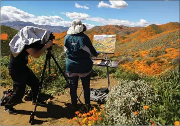  ?? MARIO TAMA — GETTY IMAGES ?? A man photograph­s a woman painting the superbloom of wild poppies blanketing the hills of Walker Canyon last week near Lake Elsinore. Thousands of tourists have descended on the area to take in the colorful sight.