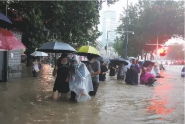  ?? Chinatopix ?? People walk through floodwater­s in Zhengzhou. Unusually heavy rains flooded the city’s subway system, and more than 10,000 residents in central China’s Henan province have been moved to shelters.