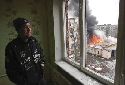  ?? PHOTOS BY YEVHEN TITOV / AP ?? A local resident stands at the window as smoke rises from a burning building after the Russian shelling in the town of Chasiv Yar, the site of the heaviest battles with the Russian troops, in the Donetsk region of Ukraine on Monday.