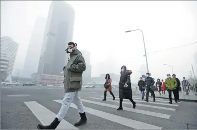  ?? JASON LEE / REUTERS ?? People wear respirator­y masks in Beijing’s central business district during December after a red alert was issued for heavy air pollution.