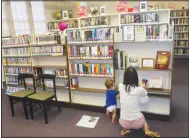  ?? (NWA Democrat-Gazette/Susan Holland) ?? Lu Hoffer of Rose, Okla., helps her son, Kang Hoffer, 8 months old, place books on a shelf during the celebratio­n. The Hoffers recently moved to Oklahoma from Sulphur Springs, where they lived next door to the library.