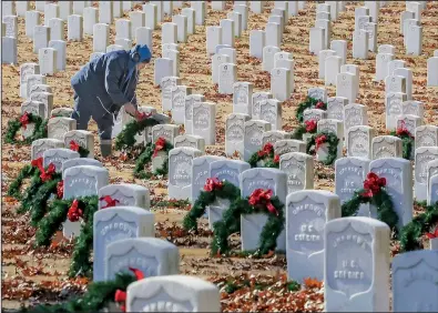  ?? Arkansas Democrat-Gazette/JOHN SYKES JR. ?? Jerron Devose, an employee of Worrell Contractor­s, places Christmas wreaths Wednesday on headstones at Little Rock National Cemetery.