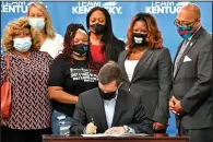  ?? (AP/Timothy D. Easley) ?? Kentucky Gov. Andy Beshear signs a bill Friday at the Center for African American Heritage in Louisville, creating a partial ban on no-knock warrants. The woman wearing the T-shirt is Tamika Palmer, mother of Breonna Taylor.