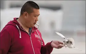  ?? (AP/Ng Han Guan) ?? Xie Yufeng (above photo), a 39-year-old cook, trains a bird using a whistle March 26 outside a stadium in Beijing. (Top photo) A wutong bird catches beads in its beak while training for a Beijing tradition that dates back to the Qing Dynasty.