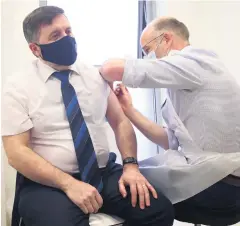  ??  ?? Robin Swann gets his vaccine from pharmacist Stephen Burns