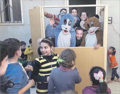  ?? Hussein Hassan Saraqeb Youth Group ?? MEMBERS OF the Saraqeb Youth Group entertain a young audience in Saraqeb, Syria, with a performanc­e featuring the cartoon characters Tom and Jerry. The all-volunteer troupe, which was formed in 2006, has continued performing throughout the Syrian civil...