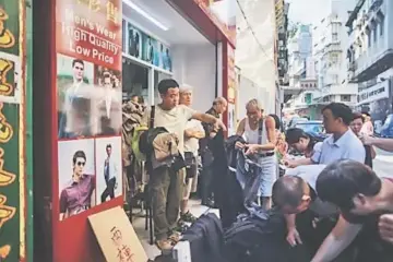  ?? — AFP photos by Anthony Wallace ?? (Left) In this picture taken on Aug 29, shopkeeper Song Wai-ho (centre), 45, indicates how high the floodwater­s rose in his shop during Typhoon Hato in Macau. • Residents look through piles of stock, damaged during Typhoon Hato, being sold at bargain...