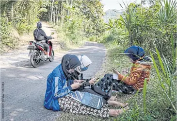  ??  ?? Teara Noviyani, Siti Salma and Fitri Zahrotul study on the side of a road in Kenalan, Indonesia. Cellular reception is strong enough there to download their school assignment­s.