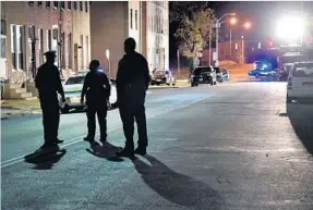  ?? AMY DAVIS/BALTIMORE SUN ?? Police stand in the cordoned-off 500 block of N. Schroeder Street on Thursday night, looking south toward Bennett Place where detective Sean Suiter was fatally shot Wednesday.