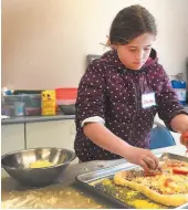  ??  ?? Dana Gronning, 9, puts the toppings on her pizza that she made at Studio 2880’s Art Monkeys ProD day camp in April. Children learned fundamenta­l art skills with some local artisans and then baked some special treats with culinary artists.