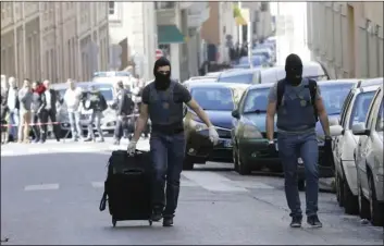  ??  ?? A hooded elite police o cers pulls a suitcase after searches in Marseille, southern France, Tuesday. The French interior minister says police have arrested two suspected radicals who were allegedly preparing an “imminent” terror attack in France as it...