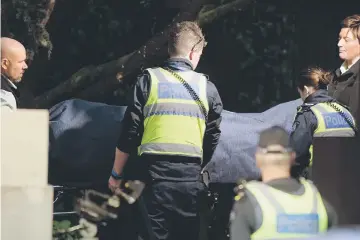  ??  ?? Police officers help the coroner remove a body at the scene of a hostage situation in the Melbourne bayside suburb of Brighton. — AFP photo