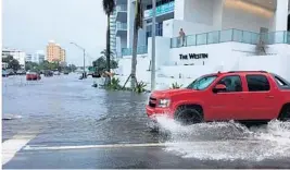  ??  ?? A car navigates a flooded street on a similarly sunny day in Sarasota, on the Gulf Coast.