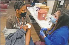  ?? (AP/Ted S. Warren) ?? Judy Jideonwo (left), a case manager at Angeline’s Day Center For Women, which is part of a YWCA shelter for women lacking housing in Seattle, holds her vaccinatio­n card after she received the first dose of the Moderna covid-19 vaccine from Aurora Artman (right), a medical assistant at Harborview Medical Center, at a vaccinatio­n clinic set up at the shelter.