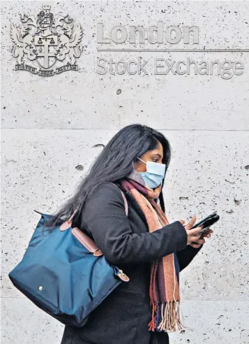  ??  ?? A woman in a face mask outside the London Stock Exchange. Economists expect the coronaviru­s to trigger a global recession