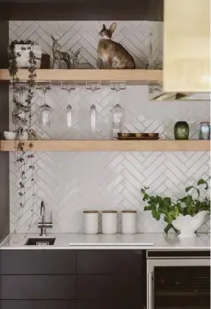  ??  ?? Annika enjoys designing kitchens that have a furniture-like quality. The matte black Bestwood Melamine cabinetry opens to reveal a drinks station featuring timber shelving and a herringbon­e tile effect. It hovers above Annika’s must-have for a modern...