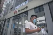  ?? MARK SCHIEFELBE­IN — THE ASSOCIATED PRESS FILE ?? On July 1, a man looks at his smartphone as he walks past a Huawei store in Beijing.