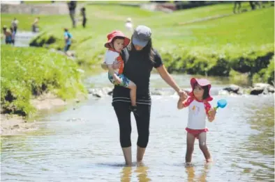  ??  ?? Monica Linares, carrying her 2-year-old son, Erick, takes a refreshing walk with her 3-year-old daughter, Bella, in a stream at Belleview Park in Englewood in July. Andy Cross, The Denver Post