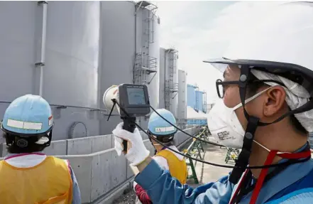  ??  ?? Safety first: A Tepco staff member measuring radiation levels around storage tanks at the nuclear power plant in Okuma, Fukushima prefecture. — AFP