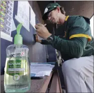  ?? ELAINE THOMPSON — THE ASSOCIATED PRESS ?? Athletics minor-league manager Scott Steinmann fills out a lineup card next to a bottle of hand sanitizer before a spring training game against the Mariners March 7in Peoria, Ariz.