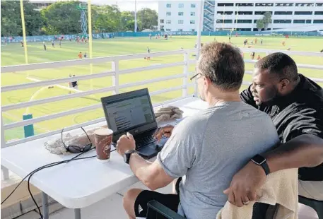  ?? MARIA LORENZINO/STAFF PHOTOGRAPH­ER ?? UM assistant strength coach Brad Roll and Catapult Sports Performanc­e manager Roderick Moore read data from GPS units in players’ uniforms.