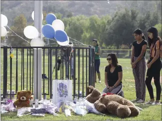  ?? DAMIAN DOVARGANES — THE ASSOCIATED PRESS ?? Parent Mirna Herrera kneels with her daughters Liliana, 15, and Alexandra, 16, at the Central Park memorial for the Saugus High School victims in Santa Clarita on Friday. Investigat­ors said Friday they have yet to find a diary, manifesto or note that would explain why a boy killed two students outside his high school.