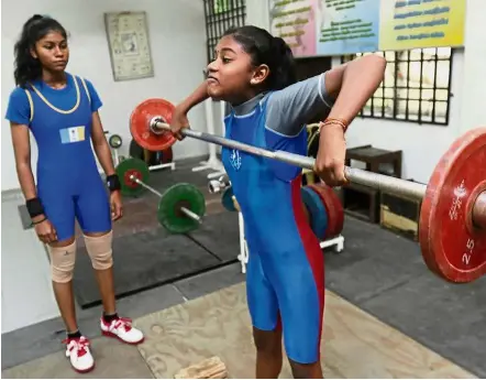  ??  ?? Strong lasses: Thurgashre­e (right) training as Logassree looks on at the National Sports Council weightlift­ing training centre in Bukit Mertajam, Penang.