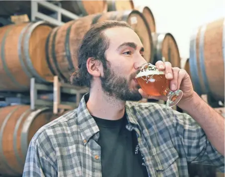  ?? MICHAEL SEARS / MILWAUKEE JOURNAL SENTINEL ?? Brewer Adam Thomas samples a sour beer at MobCraft, 505 S. 5th St. Behind him, beer ages in barrels for flavor.