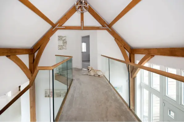  ??  ?? Above: The galleried landing overlookin­g the spacious entrance hall is one of the house’s most striking design features. Exposed timber beams are a nod to the agricultur­al style of the building