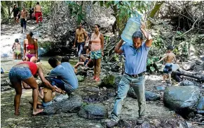  ?? GETTY IMAGES ?? A man carries a bottle filled with water while other people bathe in a river outside Venezuela’s capital, Caracas, yesterday during an electricit­y blackout which cut power to the city’s water pumps.