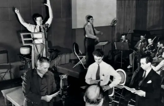  ?? ?? Une répétition de La Guerre des mondes au théâtre Mercury avec Orson Welles (à gauche les bras levés), Bernard Herrmann, qui dirige l’orchestre radiophoni­que de la CBS, et aux micros les acteurs Ray Collins et Richard Wilson (en chemise blanche).