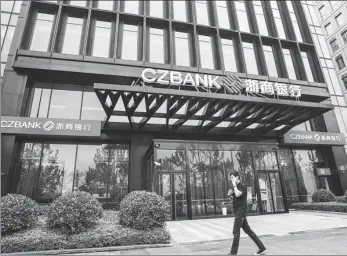  ?? LYU LIANG / FOR CHINA DAILY ?? A pedestrian walks past a Shanghai branch of China Zheshang Bank Co Ltd, a joint-stock commercial lender headquarte­red in Hangzhou, capital of Zhejiang province.