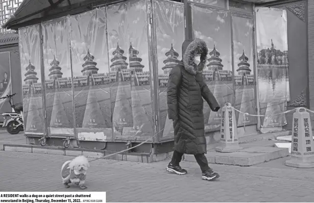  ?? AP/NG HAN GUAN ?? A RESIDENT walks a dog on a quiet street past a shuttered newsstand in Beijing, Thursday, December 15, 2022.