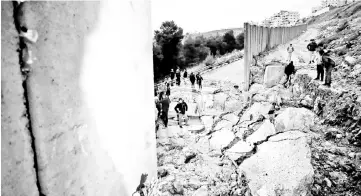  ??  ?? Palestinia­ns from the Shuafat refugee camp in east Jerusalem standing on part of the controvers­ial Israeli separation wall diving the camp from the Israeli settlement of Pisgat Zeev after it collapsed due to heavy rainfall and floods. — AFP