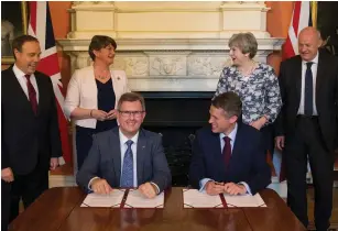  ?? (Reuters) ?? PRIME MINISTER Theresa May stands next to DUP leader Arlene Foster, as DUP MP Jeffrey Donaldson signs paperwork with Britain’s Parliament­ary Secretary to the Treasury and Chief Whip Gavin Williamson inside 10 Downing Street yesterday.