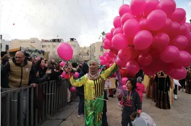  ?? (Ammar Awad/Reuters) ?? A WOMAN spreads the holiday cheer by handing out balloons at the Christmas celebratio­ns near the Church of the Nativity in Bethlehem yesterday.