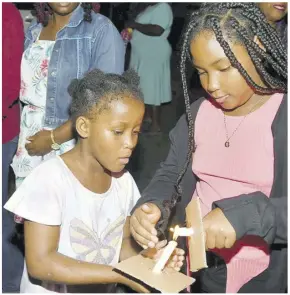  ?? (Photo: Karl Mclarty) ?? Roxana Brown (left) and Taylah Hamilton light each other’s candle at the watch night service at North Street United Church in downtown Kingston.