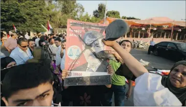  ?? Getty Images ?? An Egyptian woman hits a poster of newly elected Egyptian President Mohamed Morsi during a protest against the reinstatem­ent of the parliament in front of the tomb of the late president Anwar al-Sadaat, in Cairo, on Monday.