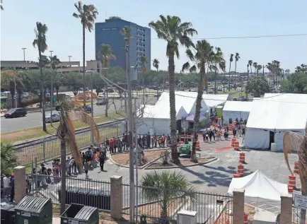  ?? PHOTOS BY ANNIE RICE/USA TODAY NETWORK ?? Migrants line up to walk to a bus station April 9 in McAllen, Texas. The tents are for coronaviru­s rapid testing before people travel to their asylum contacts.