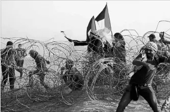  ?? ADEL HANA
THE ASSOCIATED PRESS ?? A protester uses a slingshot to hurls stones while others throw stones near the fence of the Gaza Strip border.