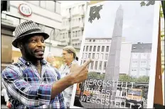  ?? DPA-BILD: UWE ZUCCHI ?? Da hoffte er noch: der amerikanis­ch-nigerianis­che Documenta-Künstler Olu Oguibe neben einem Plakat, das seinen Obelisken auf dem Platz in Kassel zeigt