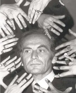  ?? AP FILE ?? In 1969, French fashion designer Pierre Cardin’s face is framed by the hands of models ornamented with a collection of rings designed by Cardin.