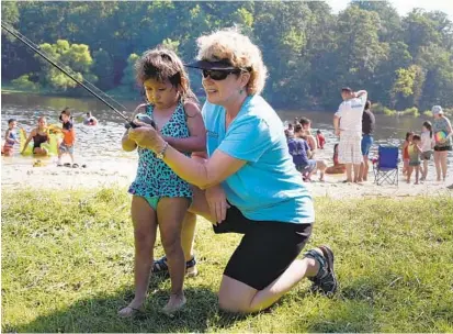  ?? BARBARA HADDOCK TAYLOR/BALTIMORE SUN ?? Scarlett Martinez, 2, of Severn, gets a fishing lesson from Dr. Linda Barker, a research statistici­an for the Maryland Fisheries Service, at Cunningham Falls State Park. State parks have seen a boost in the number of visitors in recent years.