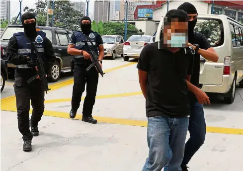  ??  ?? In custody: Police taking one of the 14 IS suspects arrested in a operation conducted by the Bukit Aman Special Branch Counter Terrorism Division that covered six states.